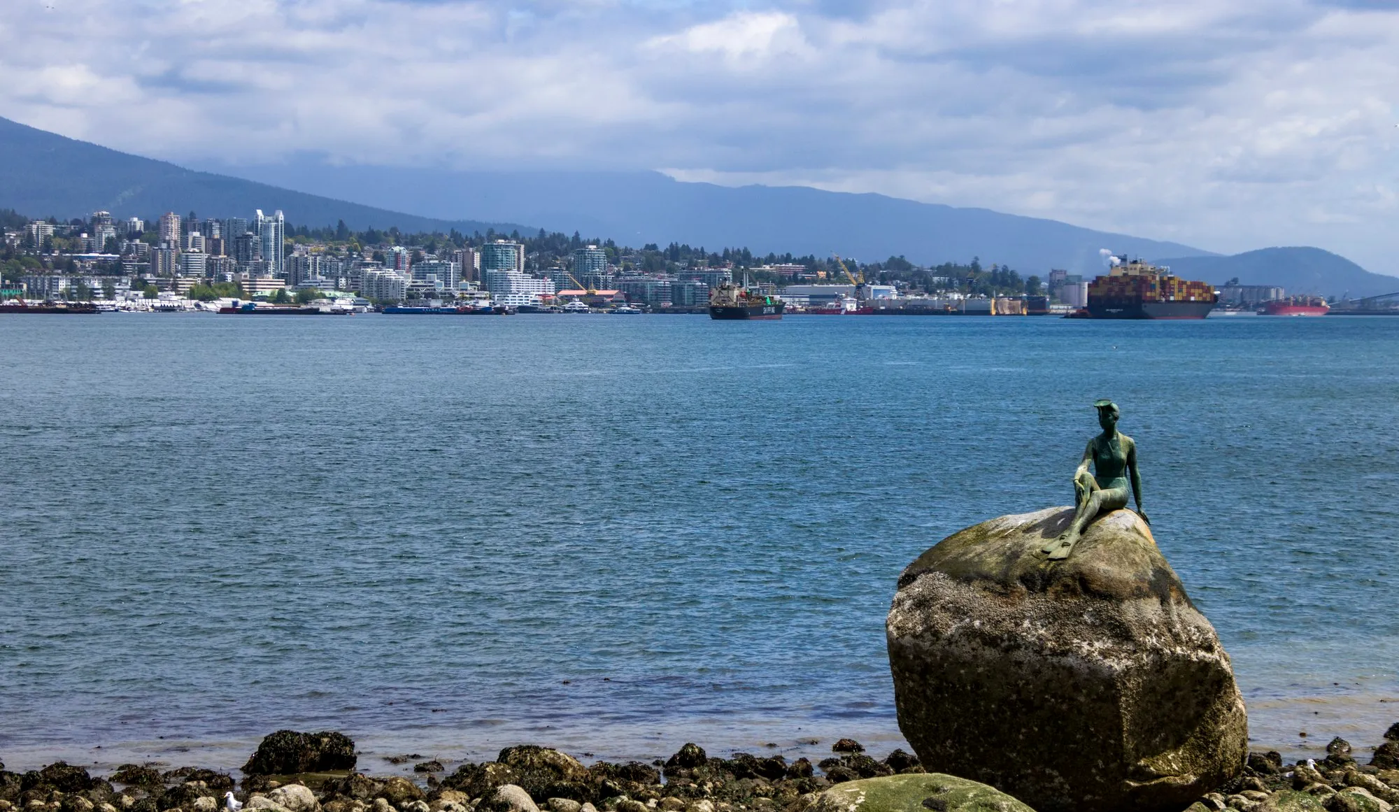 The Girl in a Wetsuit statue on its rock off the seawall, the North Shore behind it