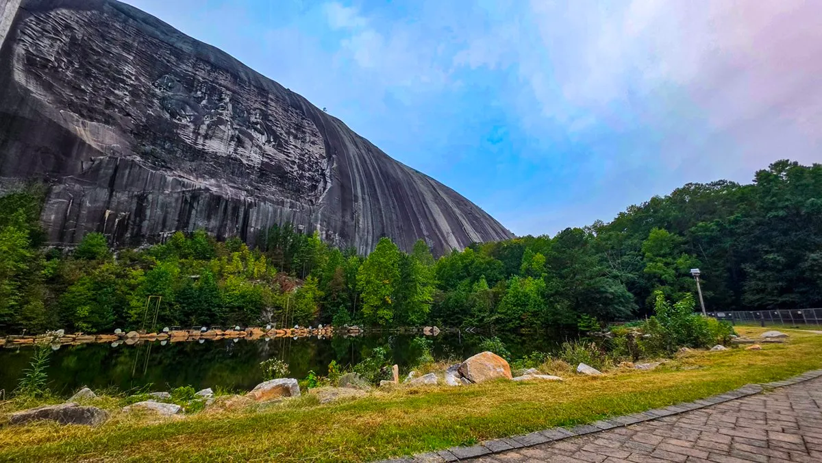 The gray north face of Stone Mountain and its carving, rising above a pond and a brick walk on a cloudy morning