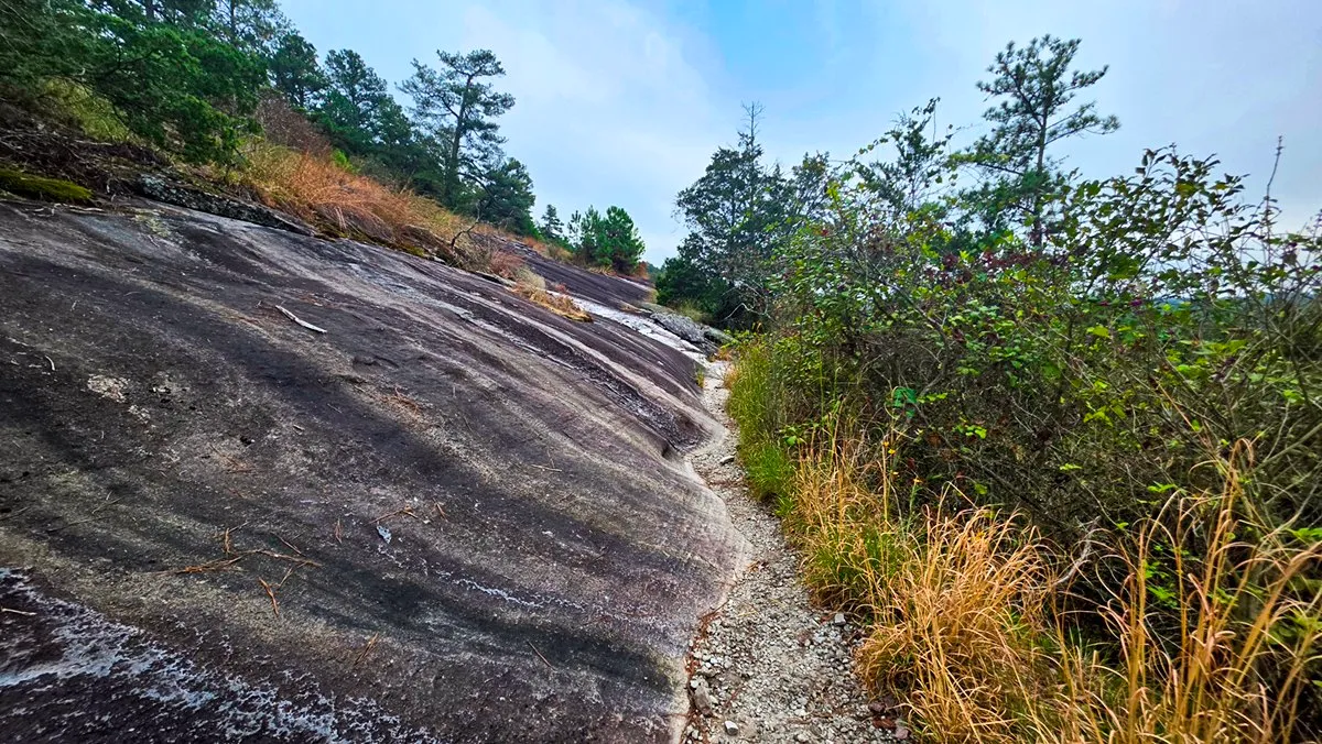 A narrow gravel path squeezed between a steep slope of granite and dense brush