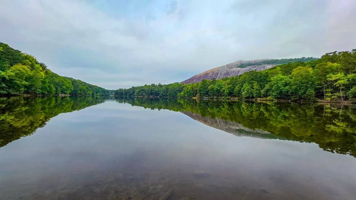 Stone Mountain reflected in the still water of Venable Lake under a cloudy sky, wooded shores on both sides