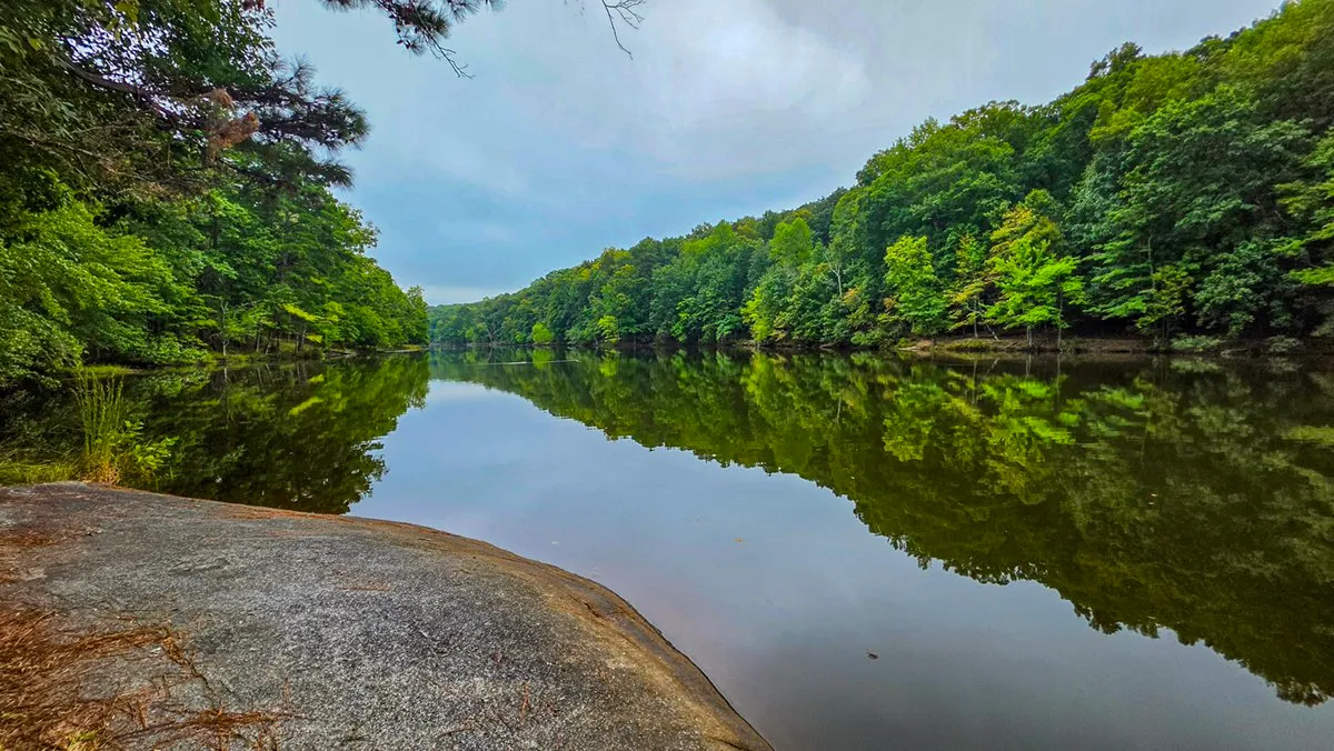 A flat granite shelf at the water's edge, the lake and the far wooded shore reflected beyond it