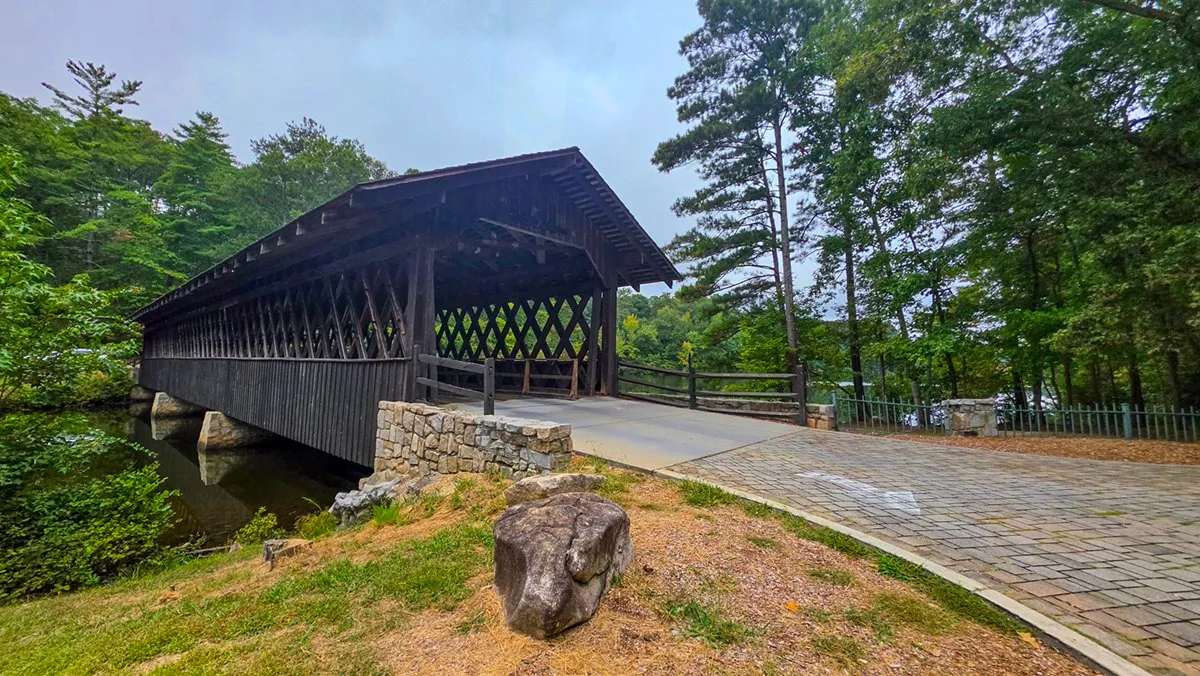 The wooden covered bridge to Indian Island beside a brick road, a boulder on the grass in front