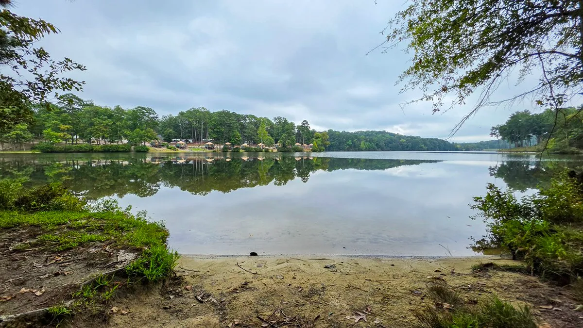 A small sandy beach at the water's edge, houses along the far shore reflected in the still lake