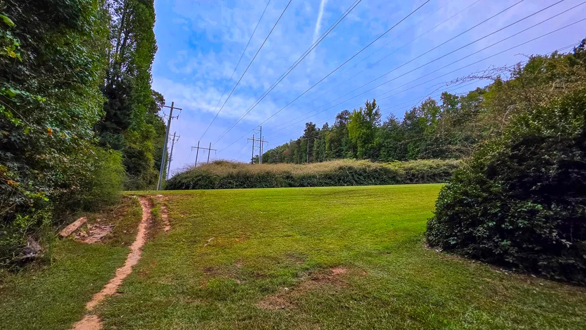 A faint footpath across the mowed grass of a power easement under the lines