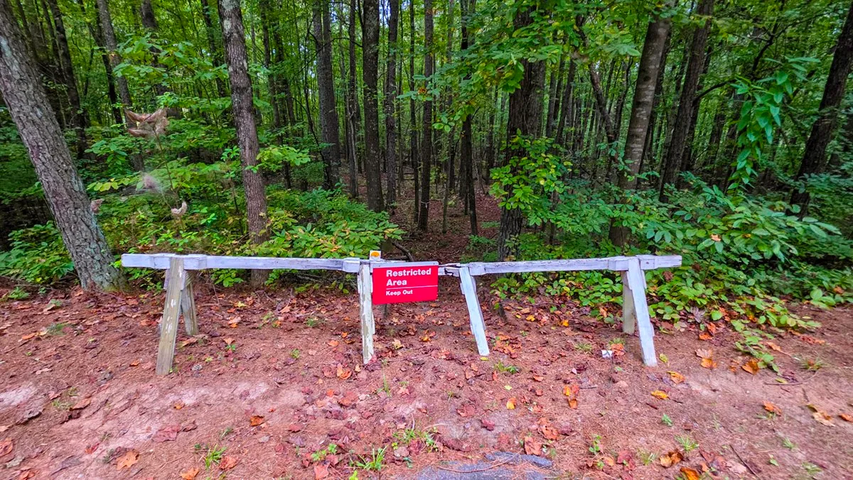 A white wooden barrier across an old path with a red Restricted Area Keep Out sign