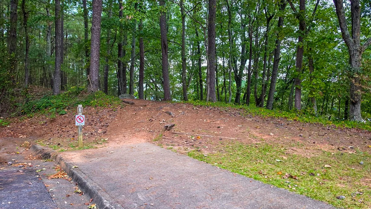A trail post with a hiker sign and a No Bicycles sign at the edge of a paved parking lot