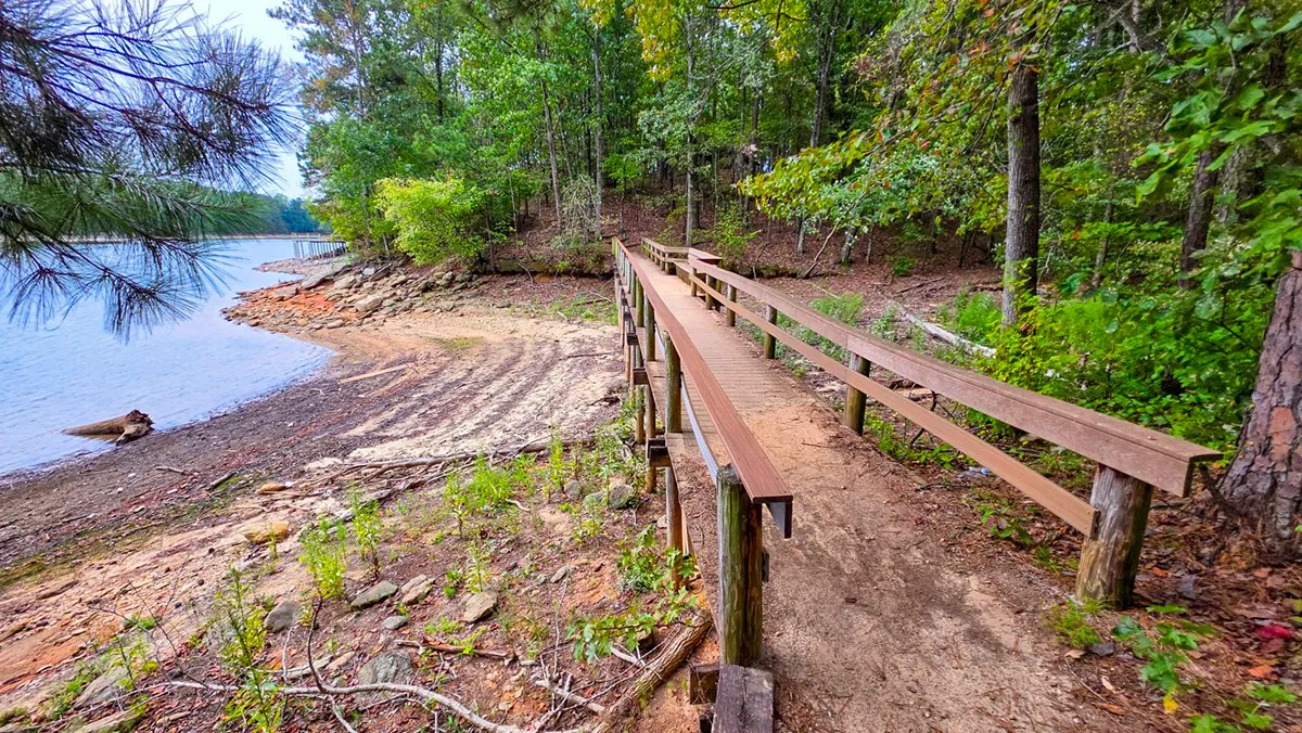 A long wooden bridge with railings running along the shore above bare rock and low water