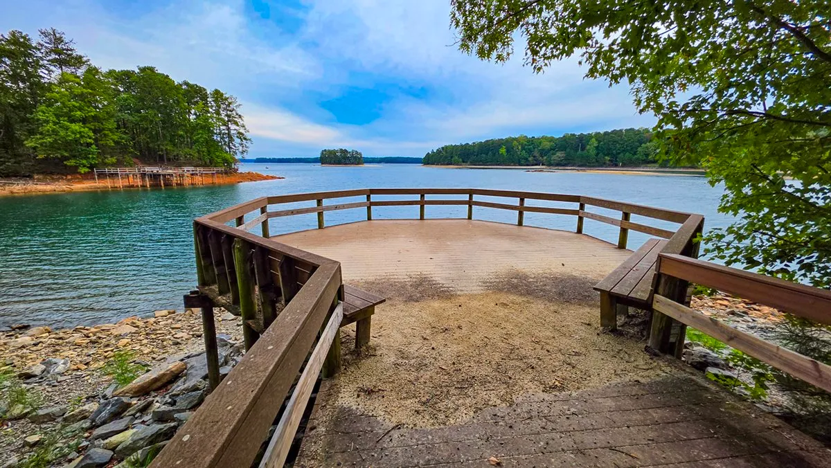 A small wooden observation deck with benches over the water, wooded shores across the lake