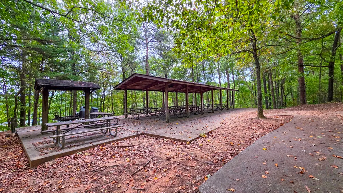 Three large picnic shelters with tables and a grill beside a paved path