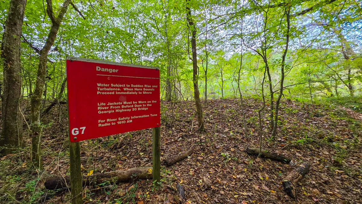A red Danger sign in the woods warning that the river below the dam can rise suddenly