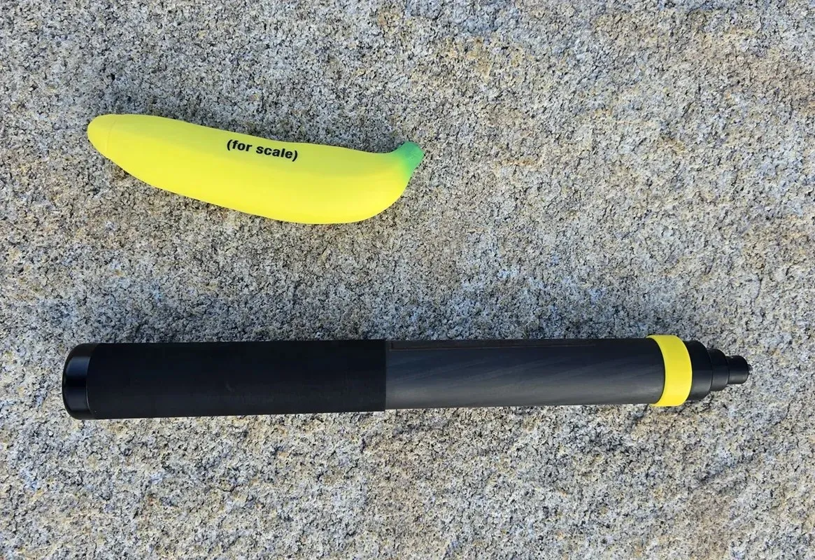 The Insta360 extended selfie stick collapsed on the granite, a toy banana marked for scale laid above it