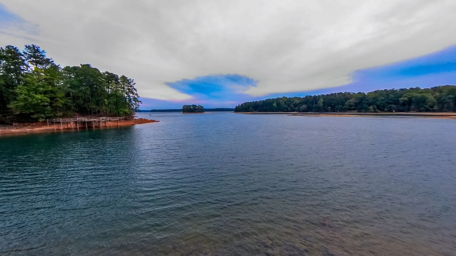 A 360 photograph from the small wooden observation deck over Lake Lanier, the railing around it, the rocky shore and the wooded points across the water