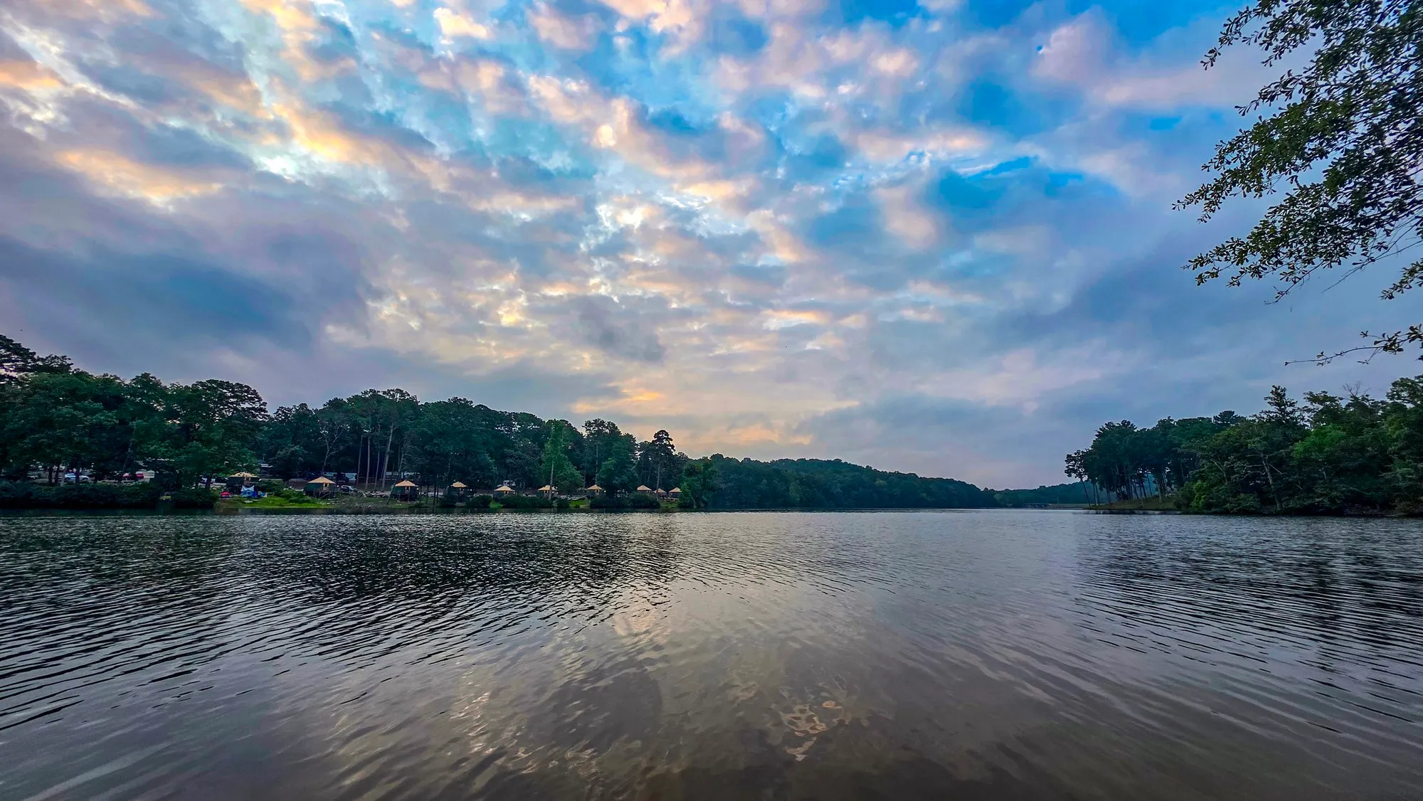 Small puffed cloud lit pink and gold after sunrise, a dock in the foreground, the lake rippled