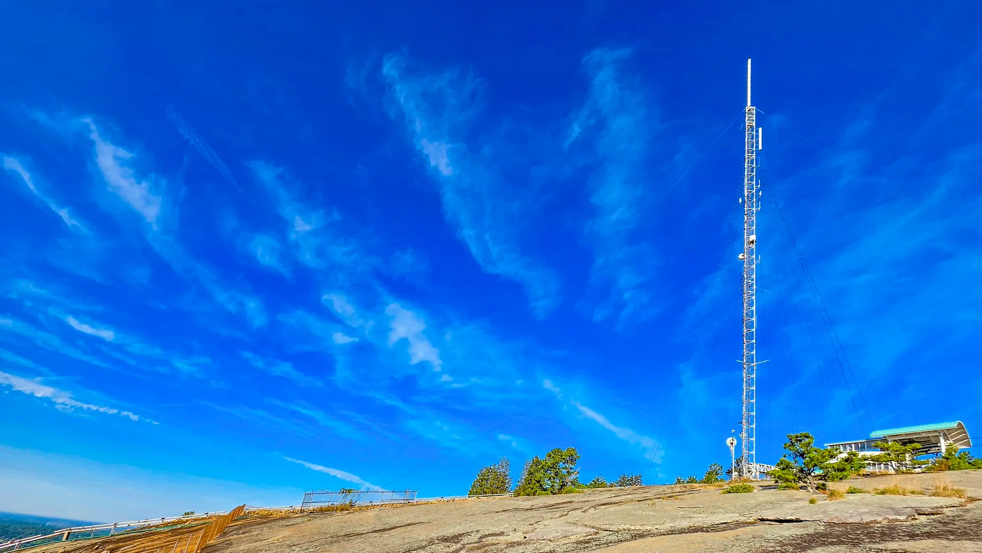 The summit's transmission tower rising from bare granite into a deep blue sky streaked with cirrus, the guy wires fanning down, the top-of-mountain building to the right