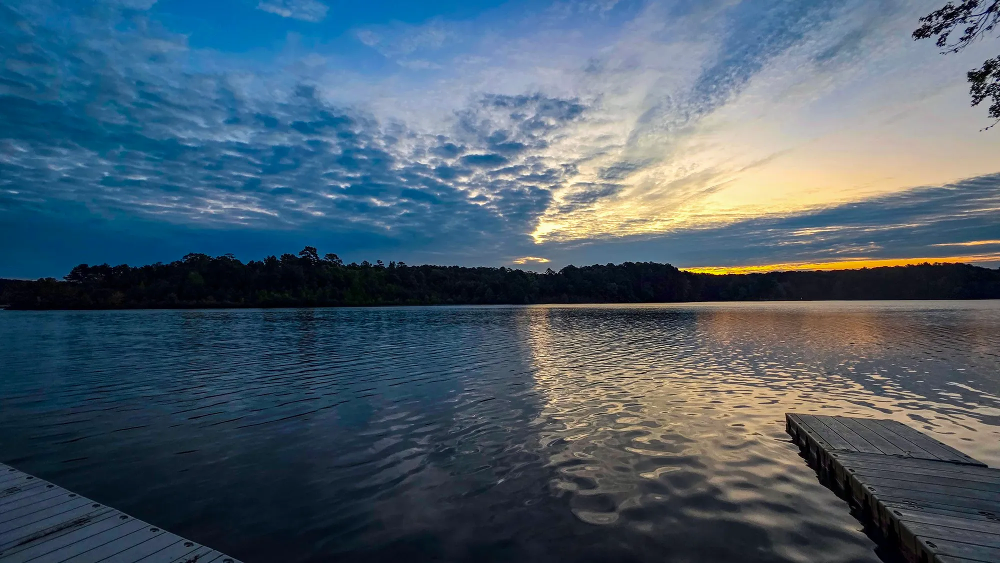 Blue sky with gray cloud over the lake before sunrise, a dock in the foreground, the water rippled