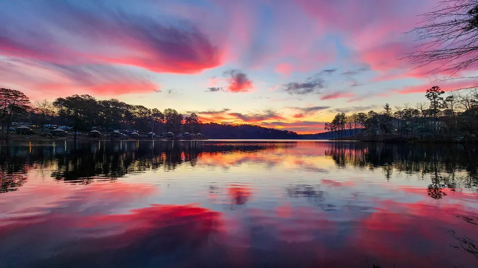 Pink and red cloud streaks fanning across the whole sky before sunrise, the lake mirroring every one, the far shore's cabins in silhouette