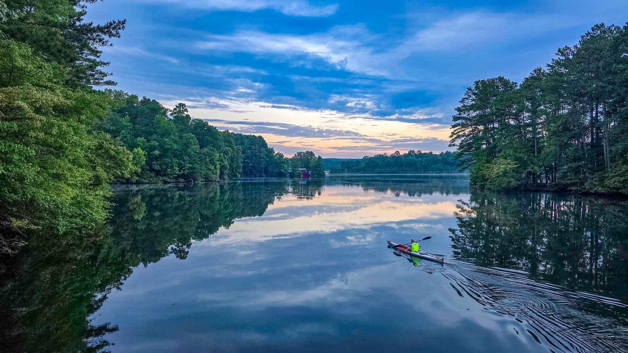 Gray cloud with a strip of blue over the lake at sunrise, a kayaker crossing the still water, wooded shores