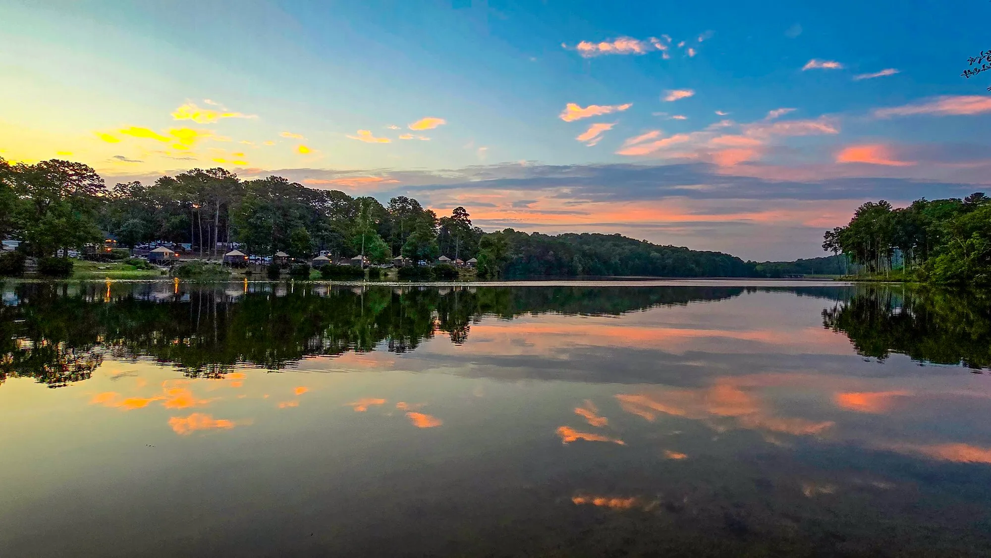 Small pink and gold clouds over the far shore before sunrise, mirrored in a still lake