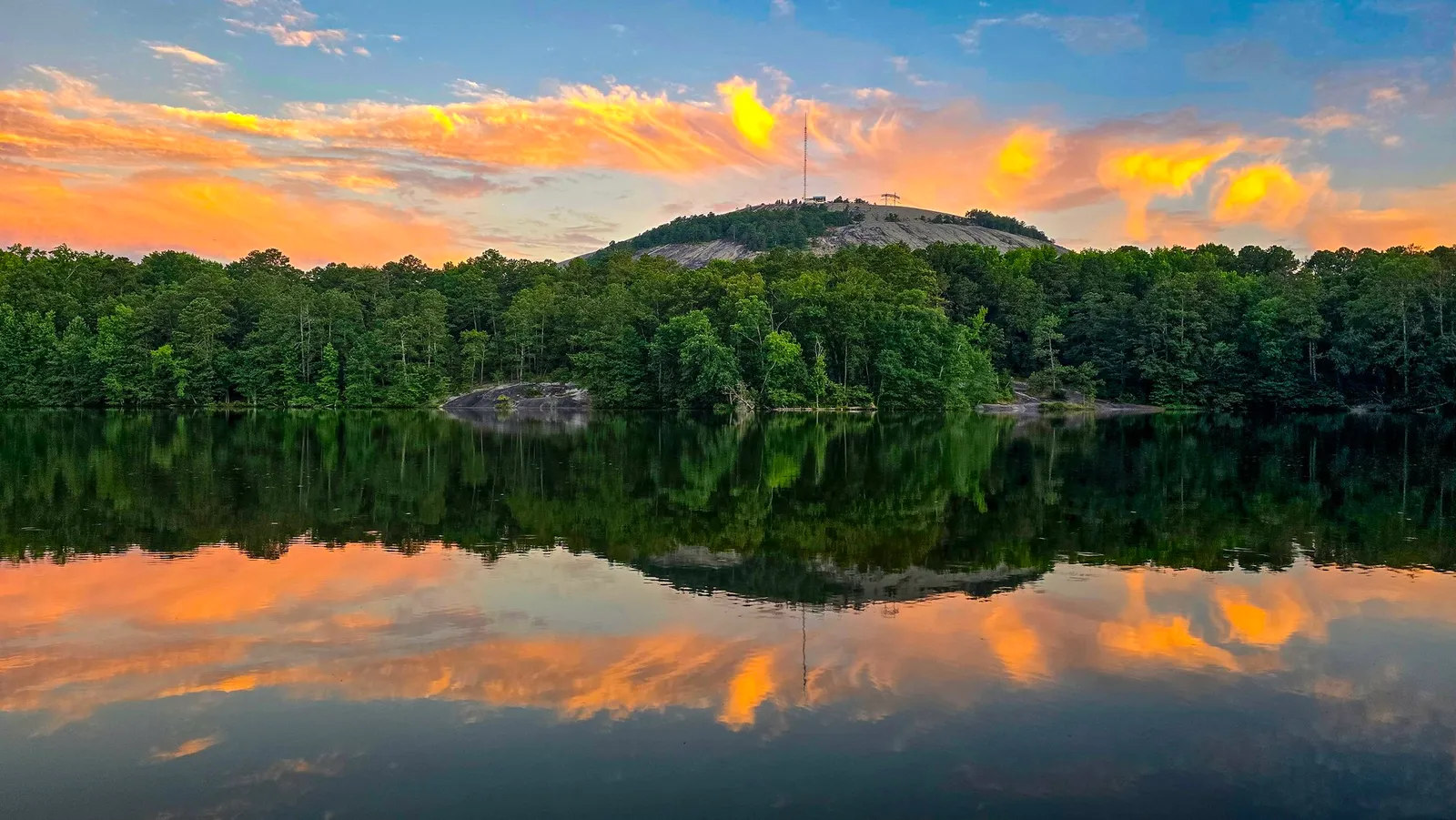 Stone Mountain's granite top above green woods under pink and gold cloud at sunrise, doubled in the still lake