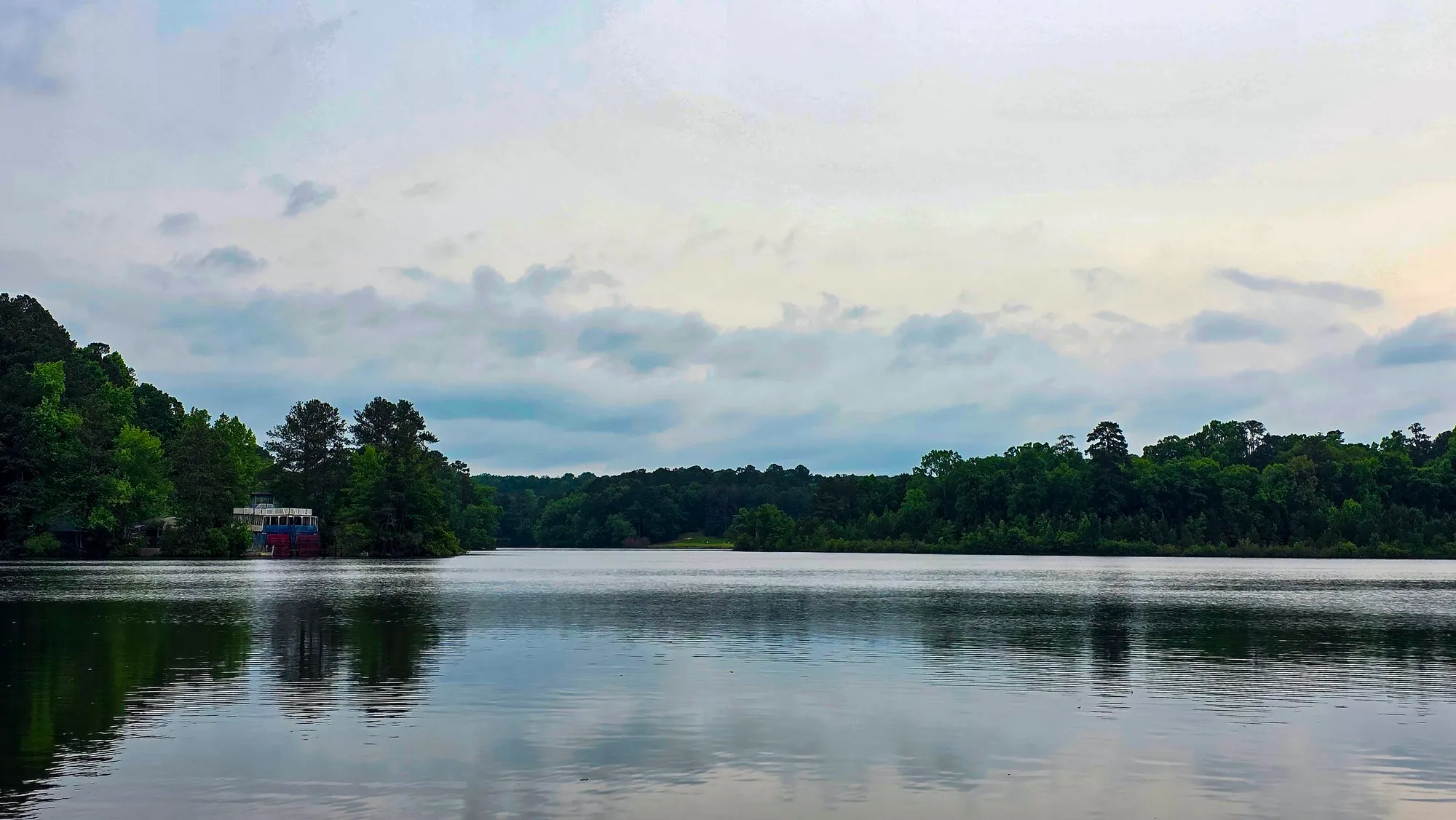 Overcast gray morning on the lake an hour after sunrise, a boathouse among the trees on the left shore
