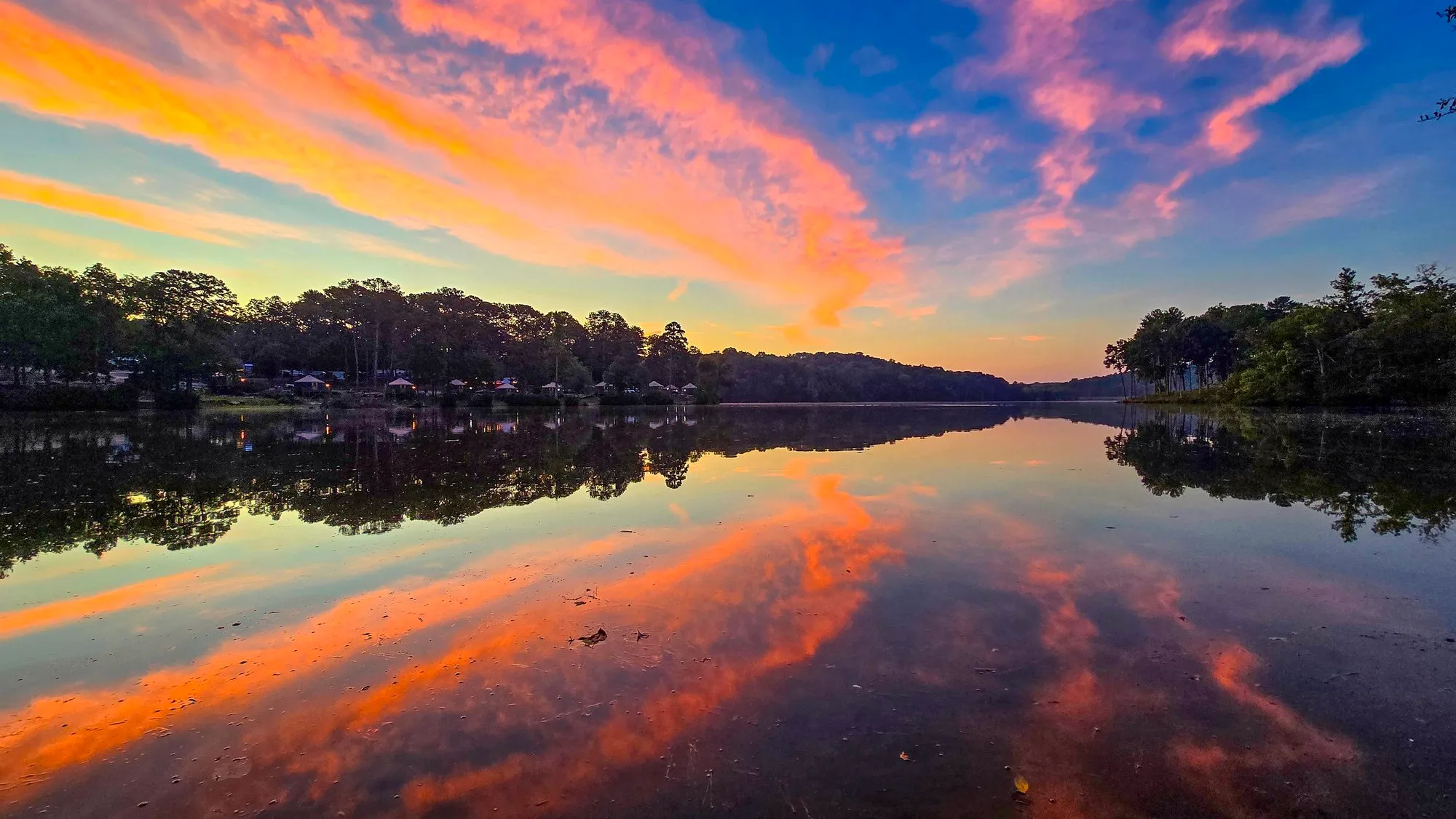 Pink and orange cloud streaks radiating over the lake before sunrise, all of it mirrored in still water