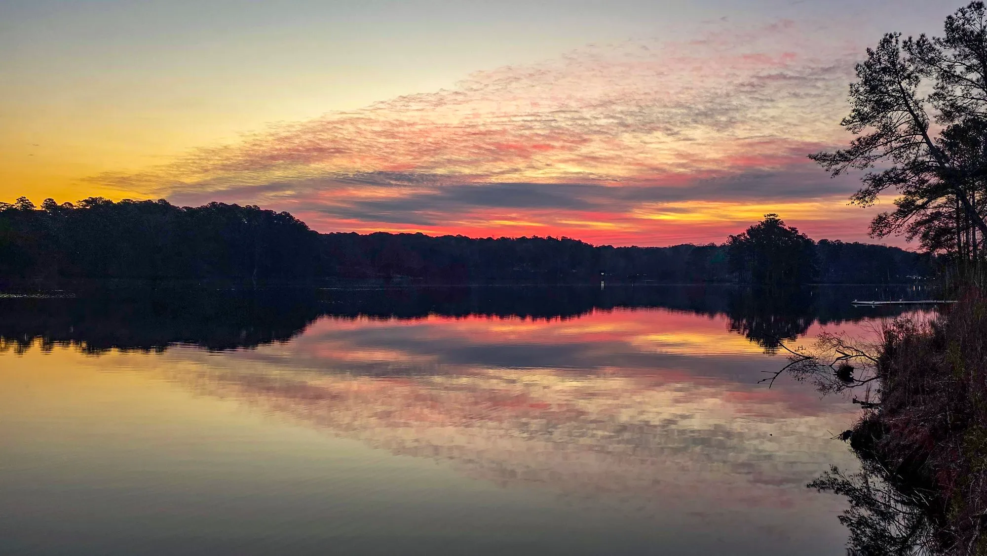 Pink and gold cloud bands fanning over the far shore before sunrise, every band mirrored in the still lake