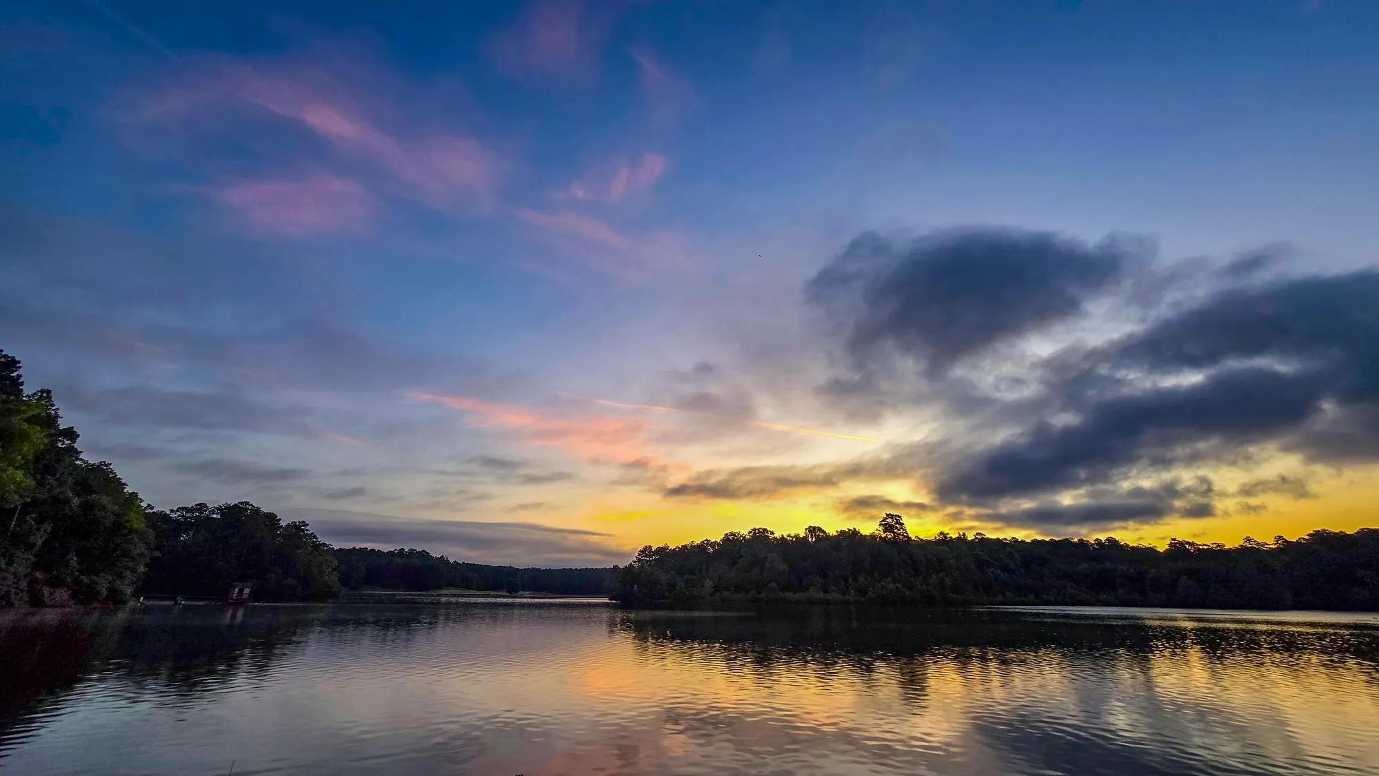 Gold light under dark cloud at sunrise over the far shore, the lake calm