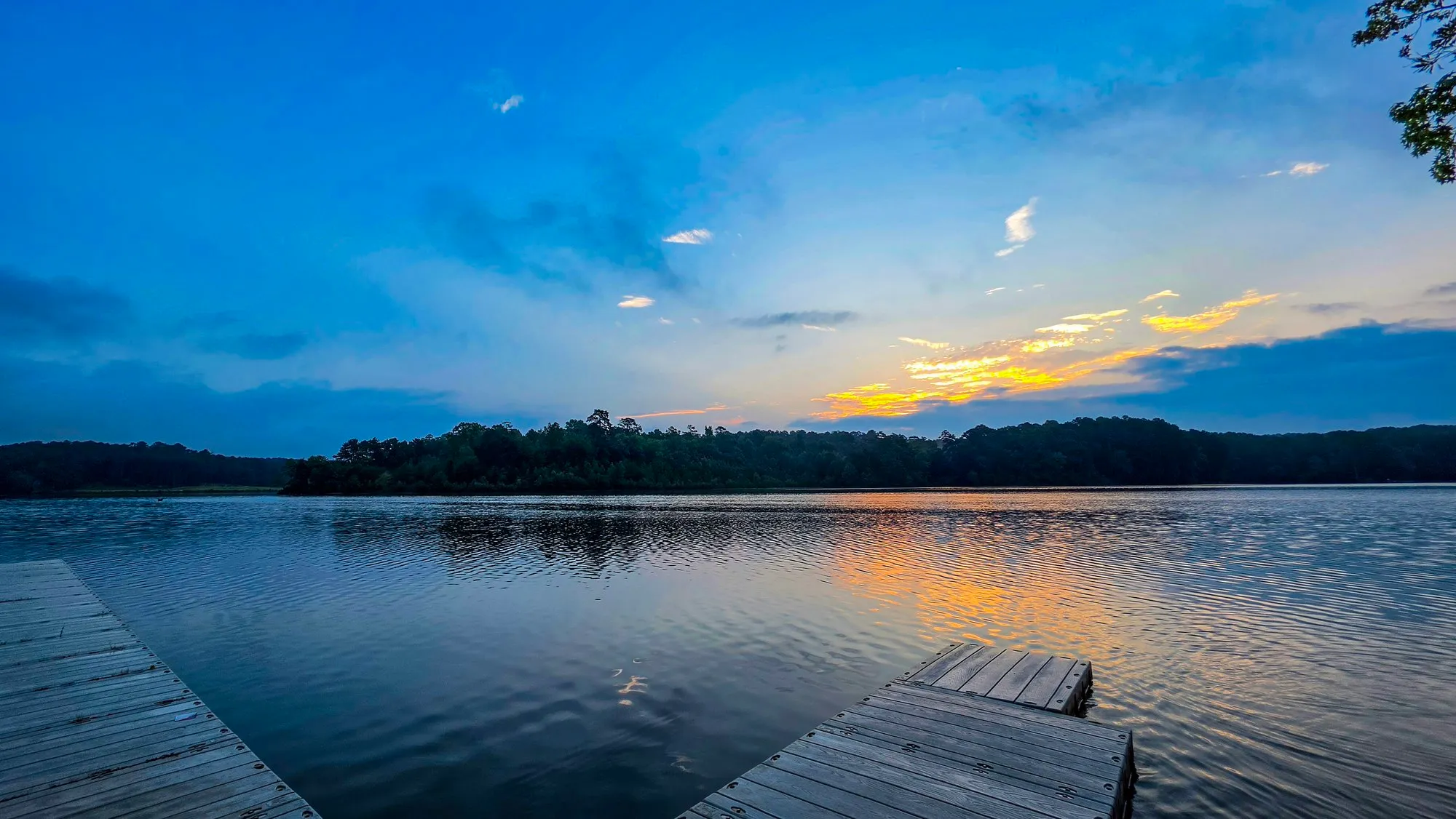 Looking out from the dock across Stone Mountain Lake, blue sky and a band of lit cloud over the far trees