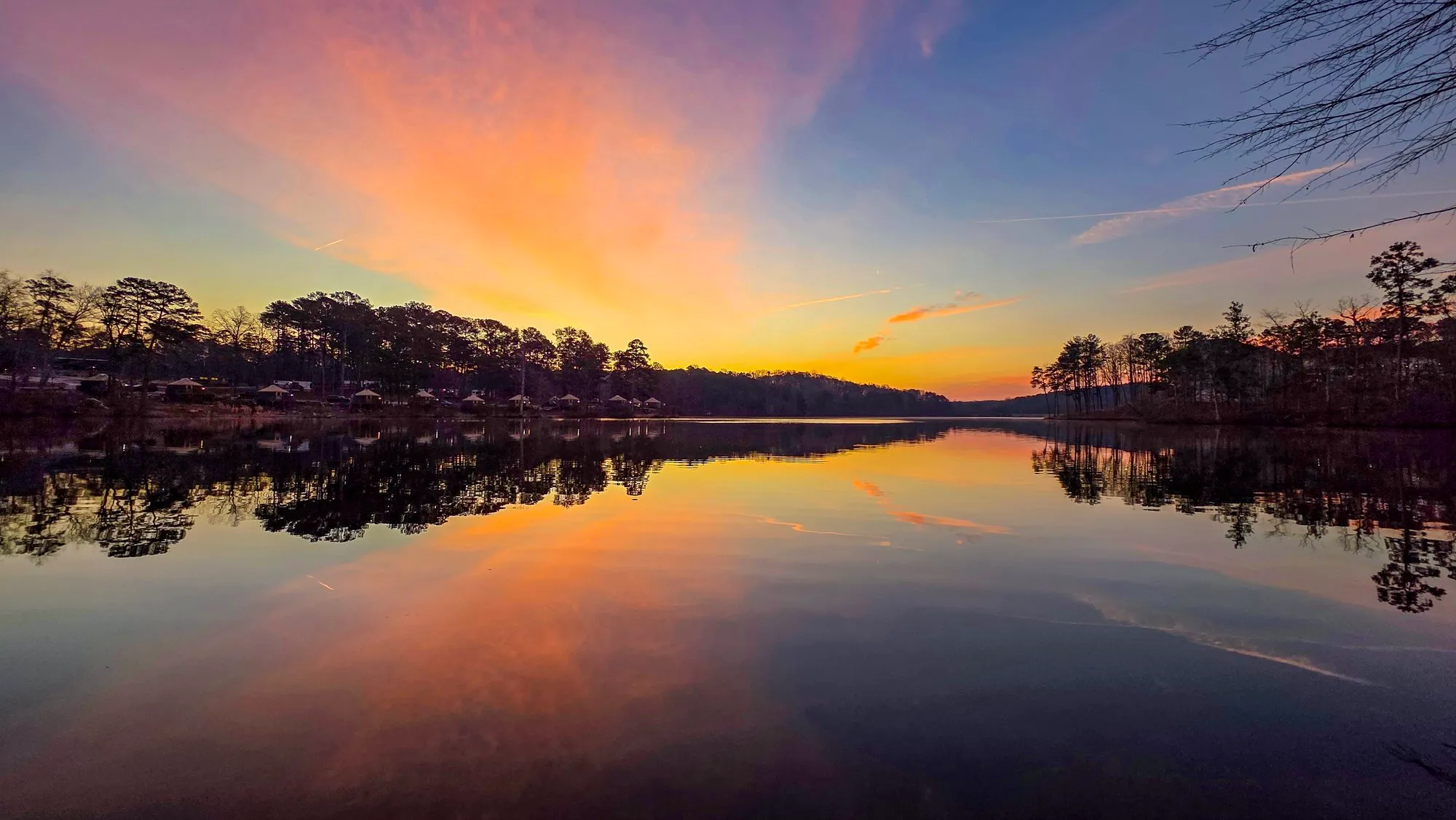 Orange and gold rays fanning up from the far shore at sunrise, a wisp of pink cloud above, the lake still enough to mirror all of it