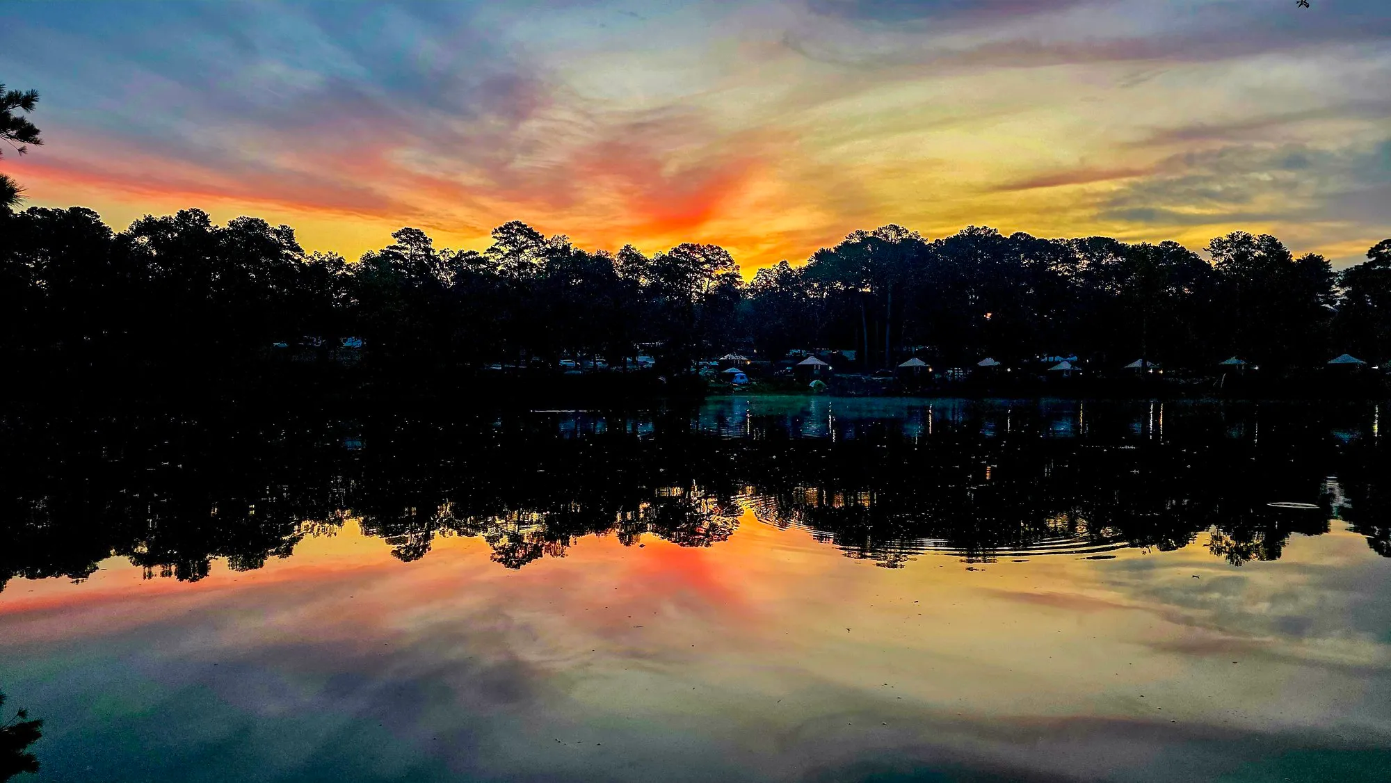 Red and gold cloud over the far shore before sunrise, the lake mirroring it, the tree line dark