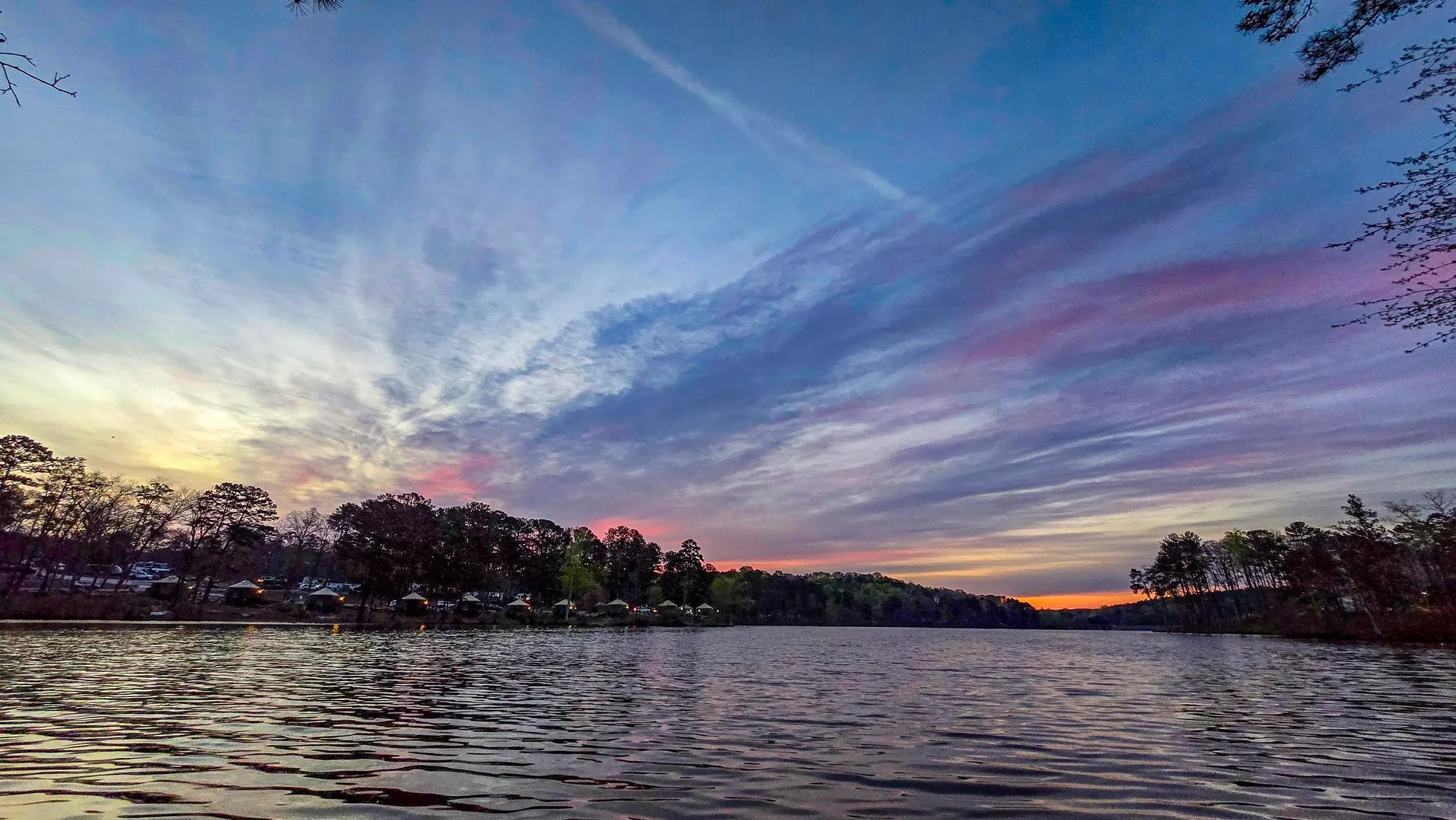 Swept gray and pink cloud filling the sky before sunrise, the far shore's trees dark, the water calm