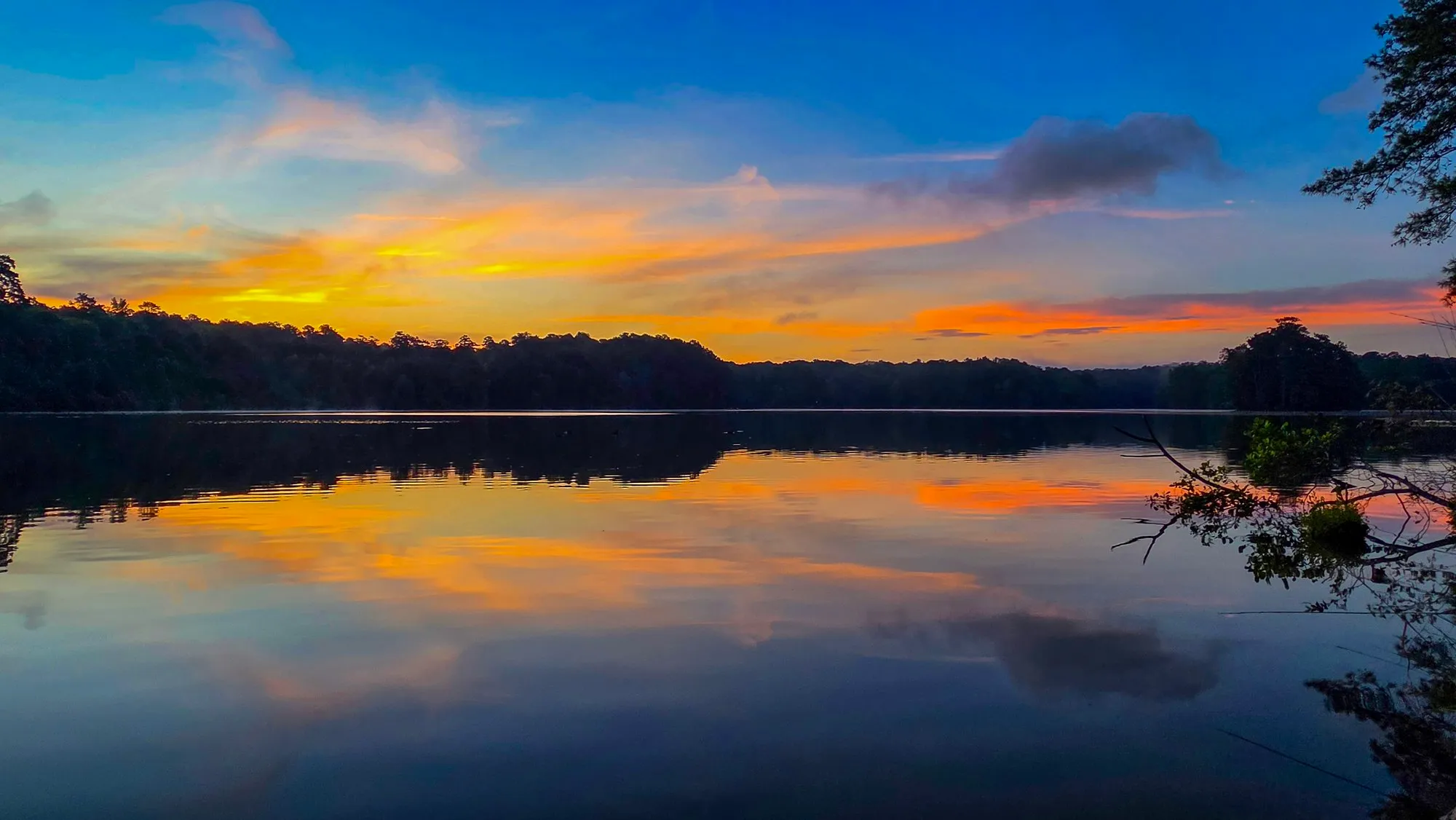 Orange and pink cloud fanning out over Stone Mountain Lake before sunrise, the far shore a dark line, the water a flat mirror