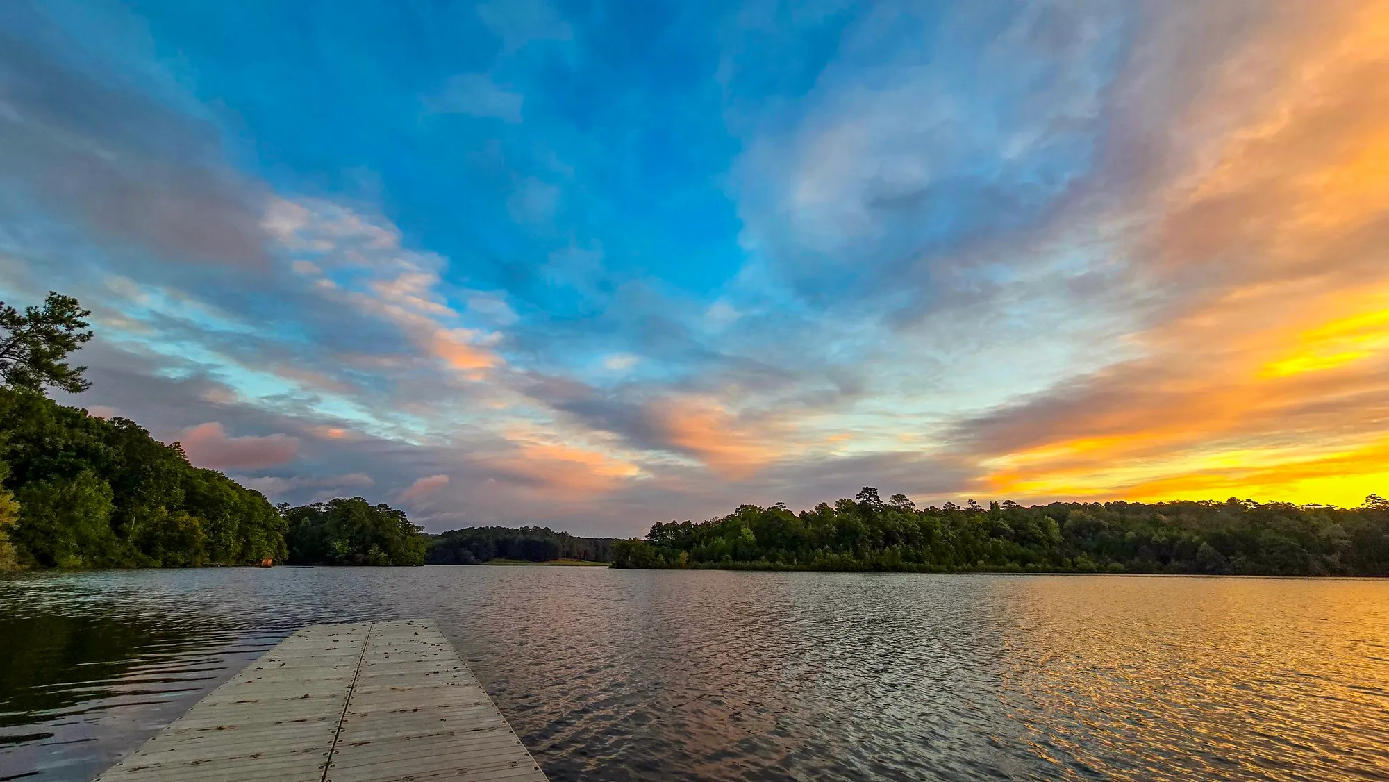 Blue sky with swept gold cloud after sunrise, a dock in the foreground, the lake rippled
