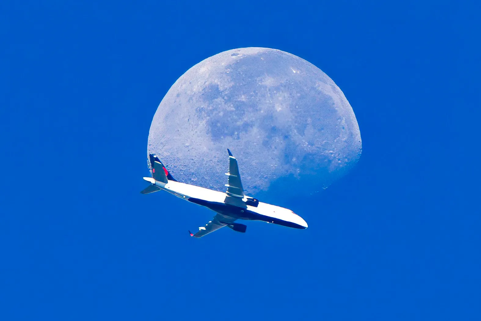 A Delta jet crossing in front of a gibbous moon in a clear blue morning sky