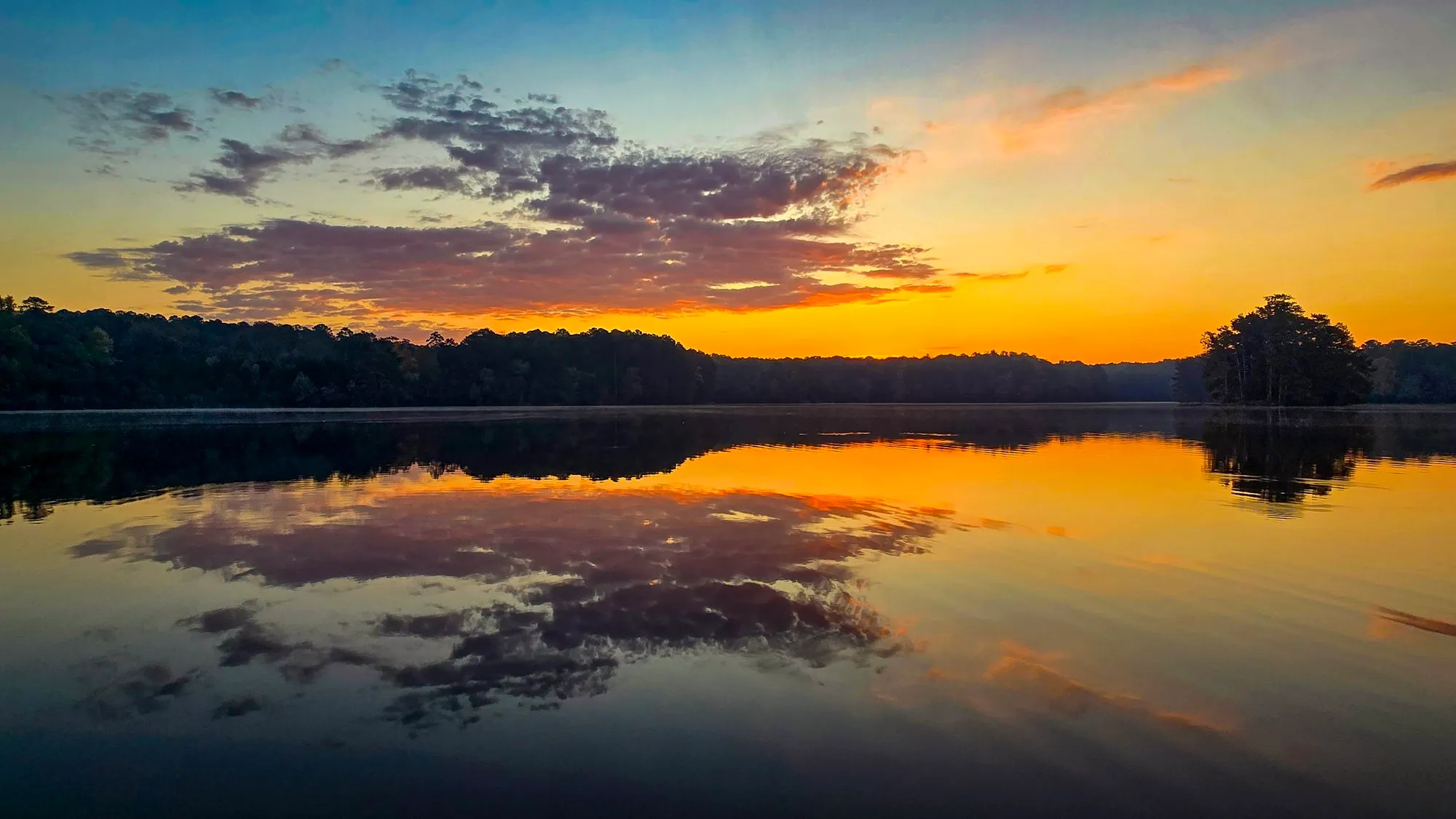 Orange dawn under a bank of purple cloud, the far shore dark, the lake still and mirroring it