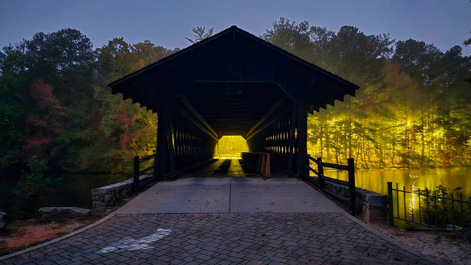 The covered bridge on the Cherokee Trail at dawn, its far end lit gold, autumn trees behind it