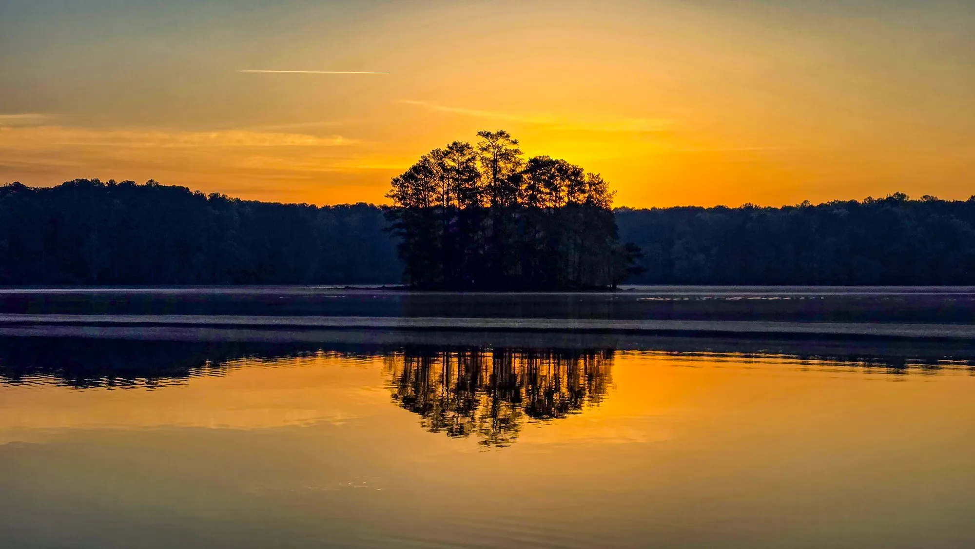 Gold haze over the lake after sunrise, a wooded island in silhouette, the water still