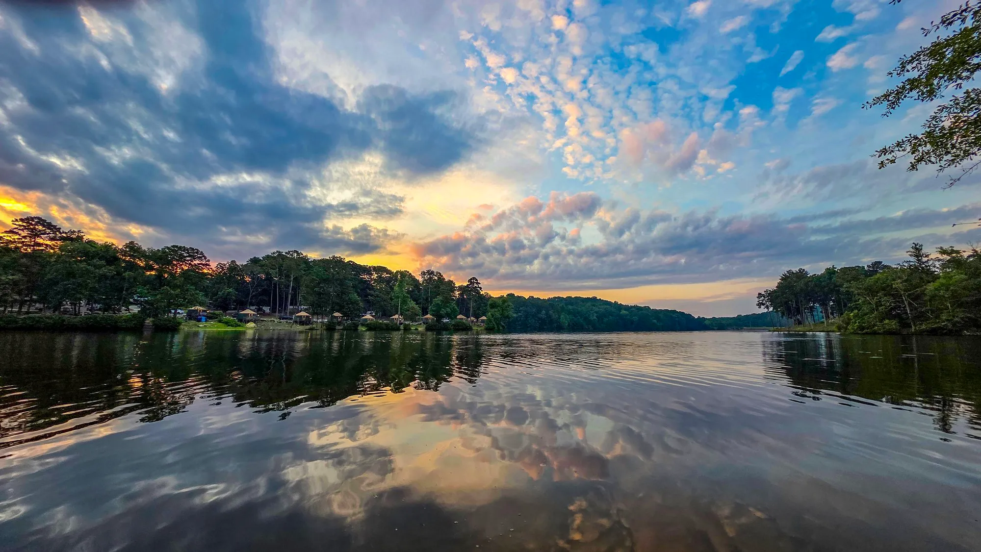 Dark cloud breaking over the lake after sunrise, pale blue sky behind, the far shore's pines lit