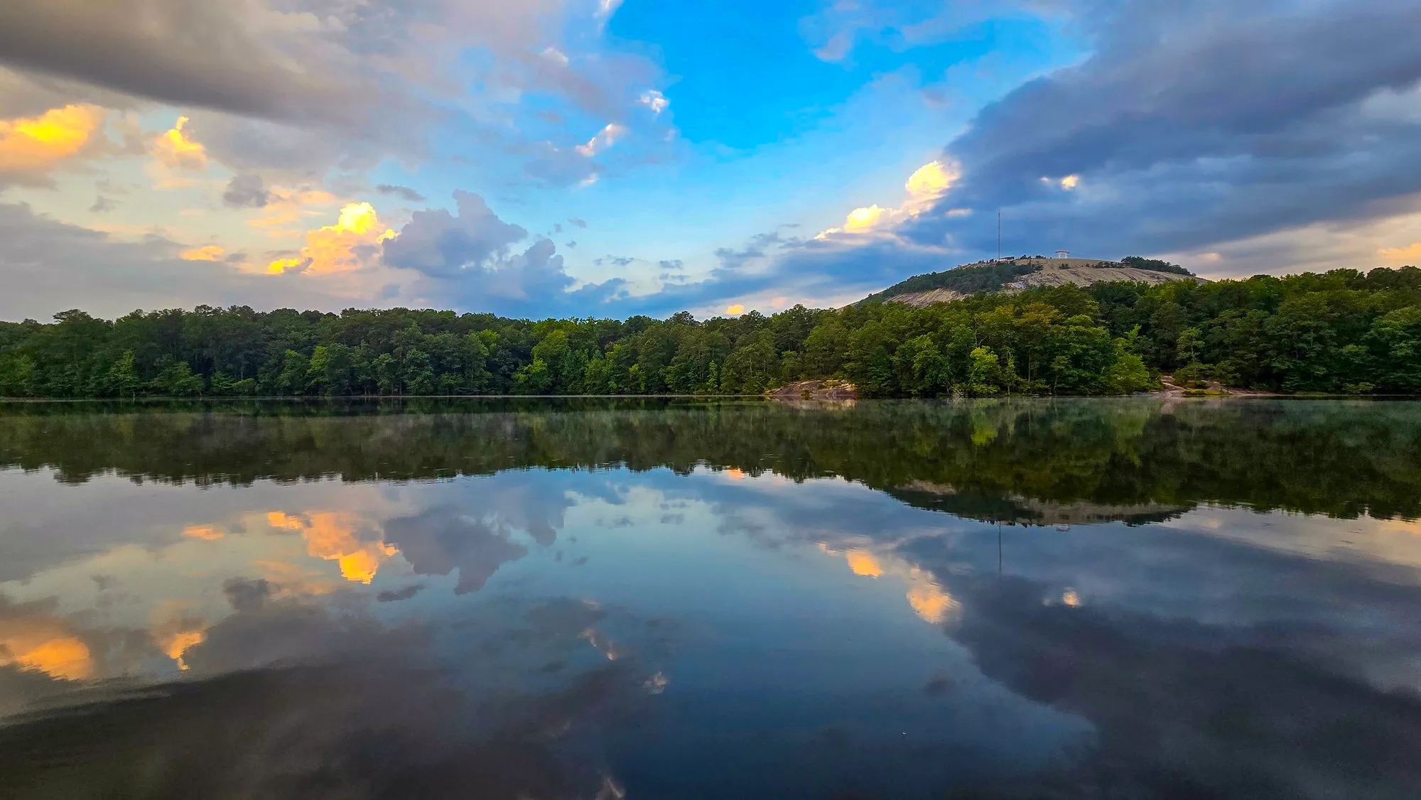 Broken gray and gold cloud over Stone Mountain's granite dome half an hour after sunrise, the lake still