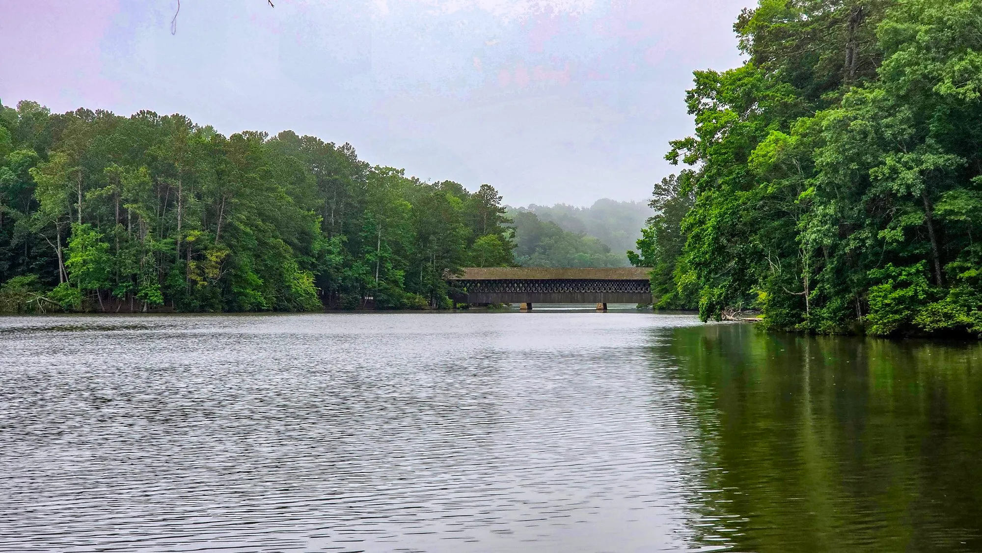 Hazy green morning on the lake, the covered bridge at the far end, trees on both shores
