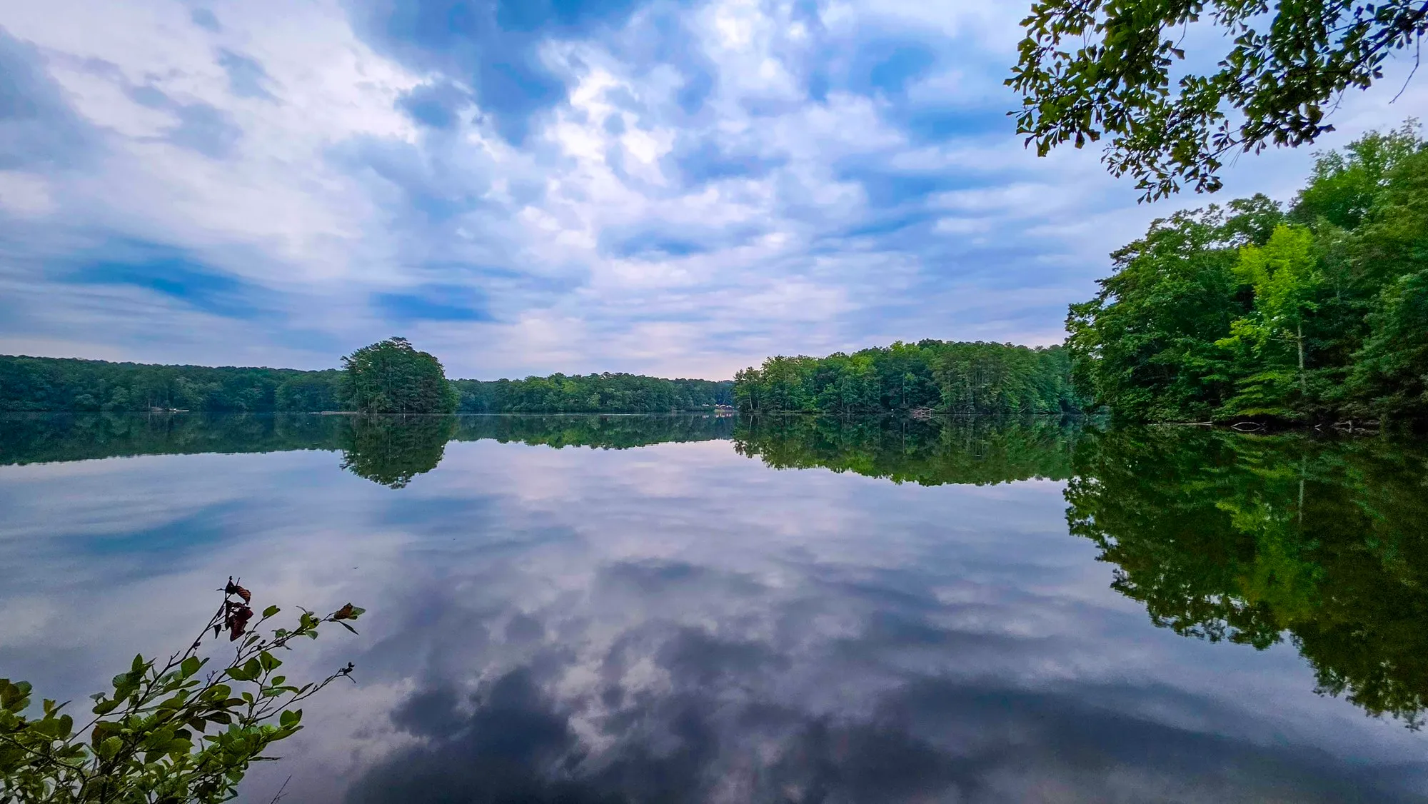 Heavy gray cloud over Stone Mountain Lake just after sunrise, a wooded island on the far side, the whole sky reflected in still water