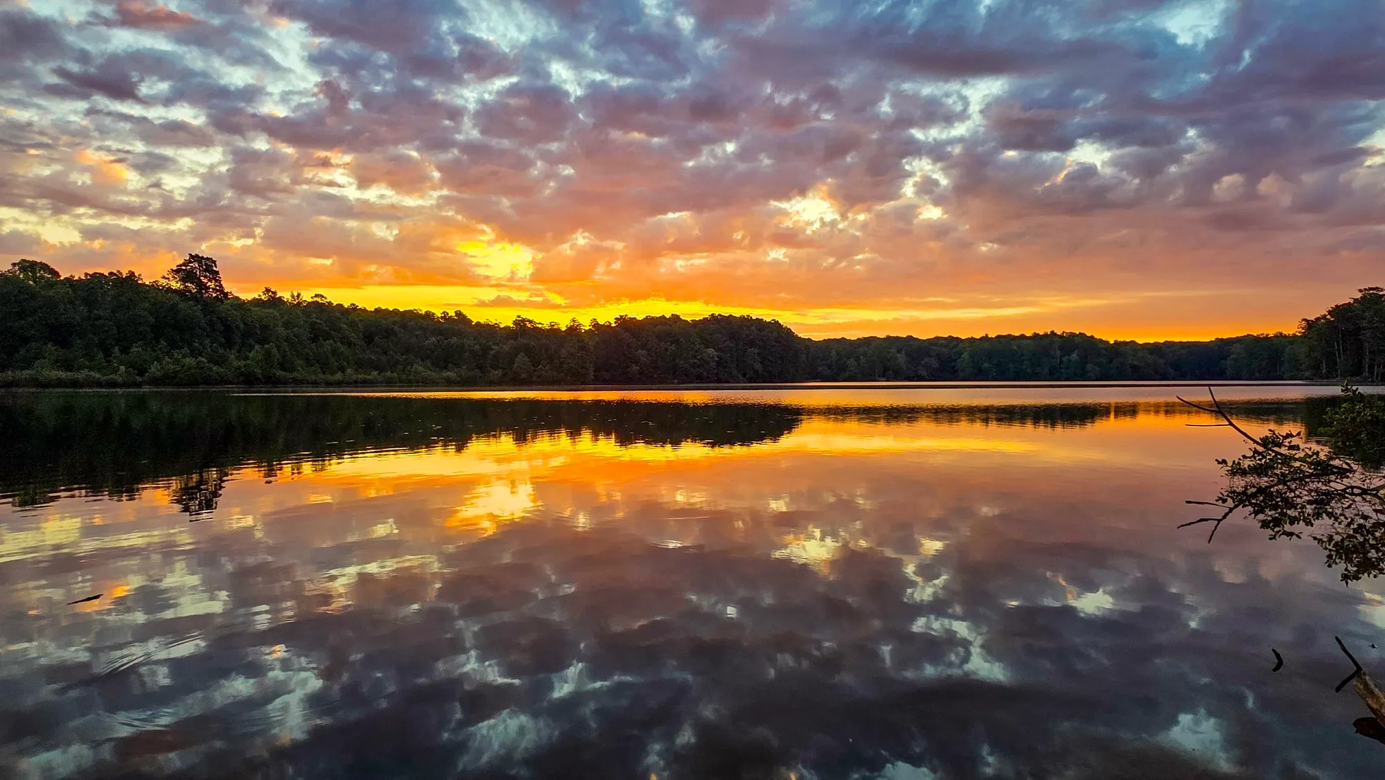 Broken gray cloud lit gold and pink after sunrise over the far shore, the lake mirroring it