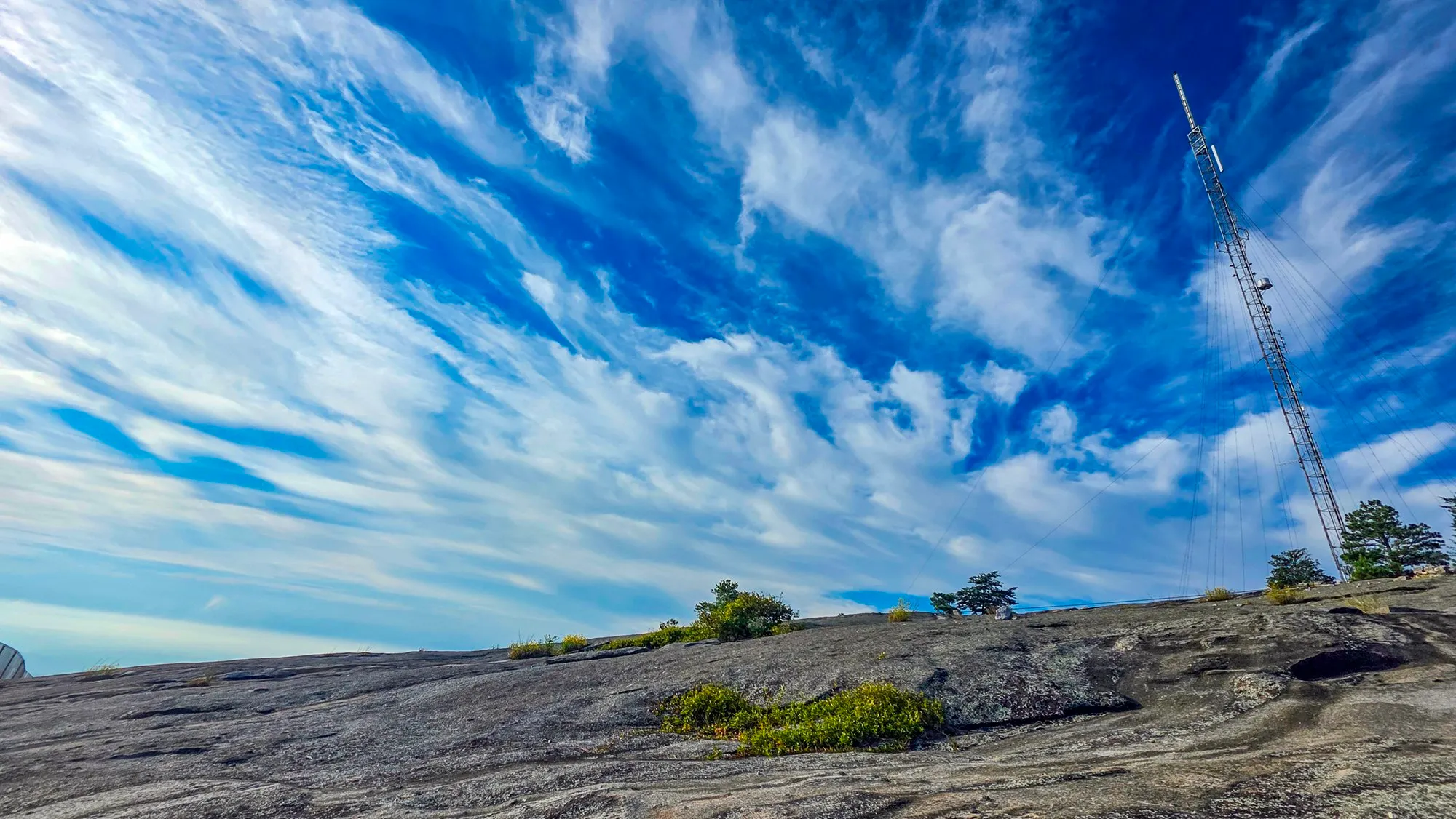 Cirrus fanned across a deep blue sky over the summit granite, the transmission tower and its guy wires on the right, low shrubs in the seams of the rock