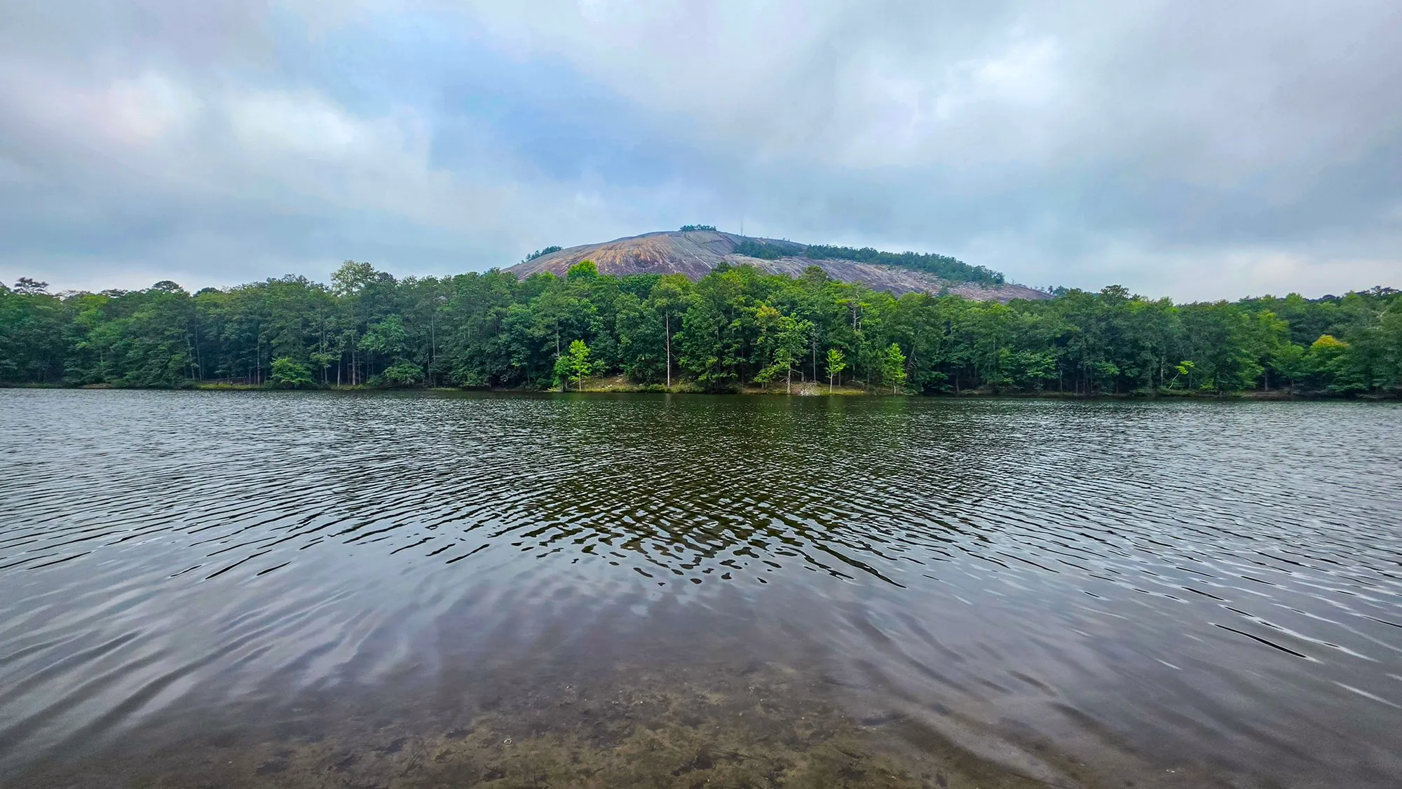 The bare granite dome of Stone Mountain above the far shore's trees across the lake, low cloud sitting on the top, the water rippled