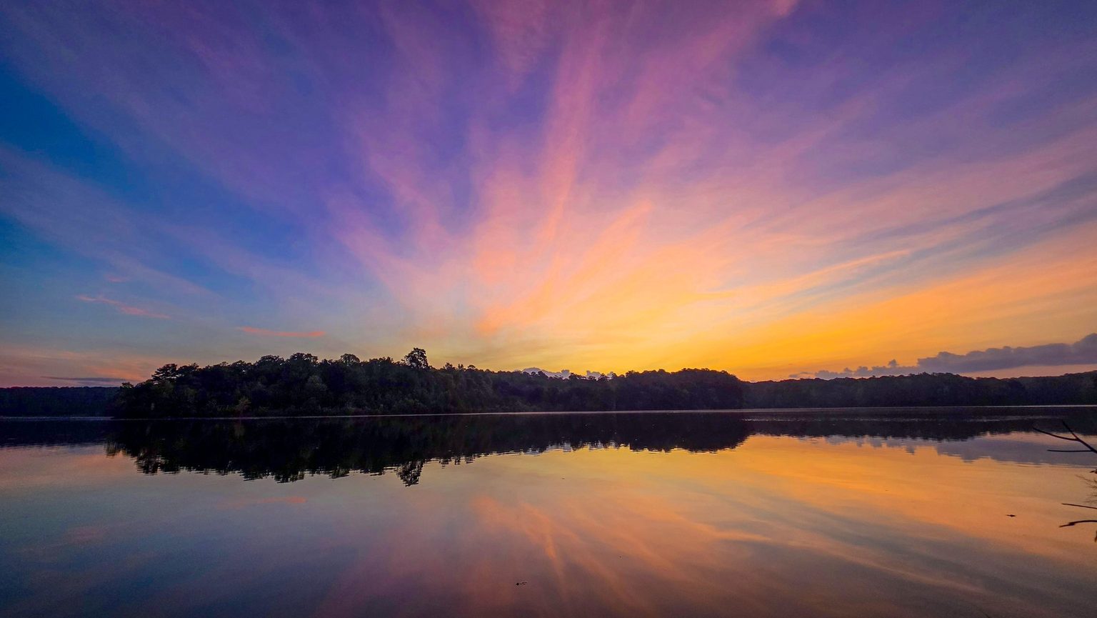 Pink and orange streaks of high cloud over Stone Mountain Lake before sunrise, mirrored in still water